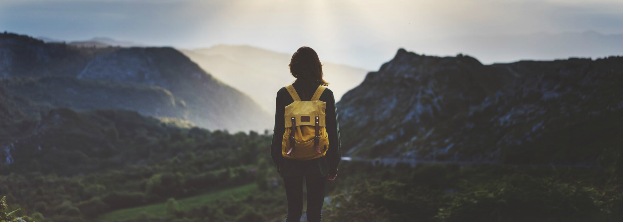 Woman standing on a mountain wearing a yellow rucksack